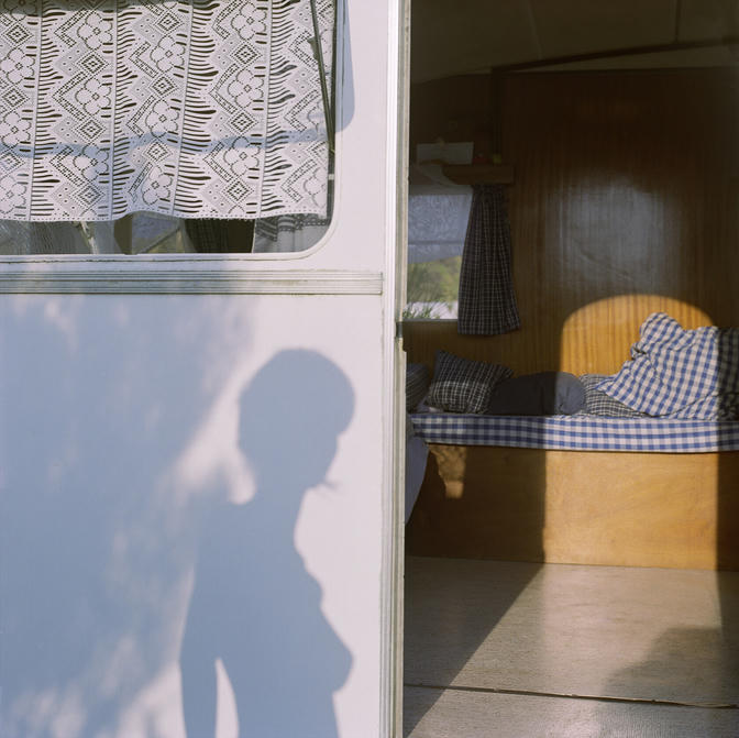 Ombre d'une femme sur une caravane dont la porte est ouverte sur une banquette avec des coussins